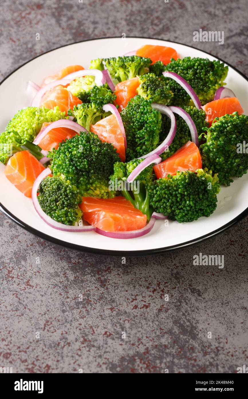 Dietary salad of steamed broccoli, salted salmon and red onion close-up in a plate on the table. Vertical Stock Photo