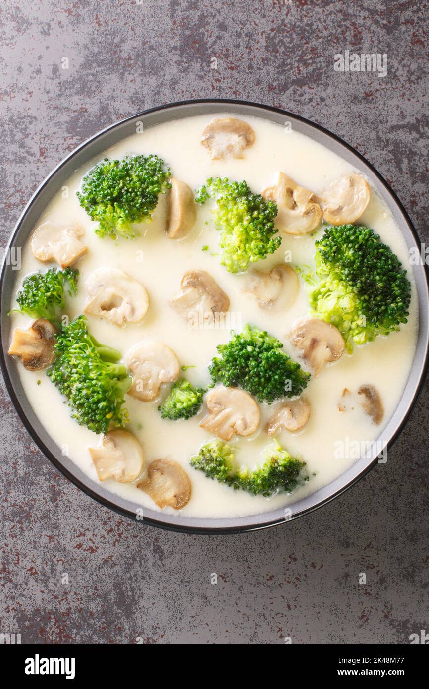 Cheesy cream soup with broccoli and mushrooms close-up in a bowl on the table. Vertical top view from above Stock Photo