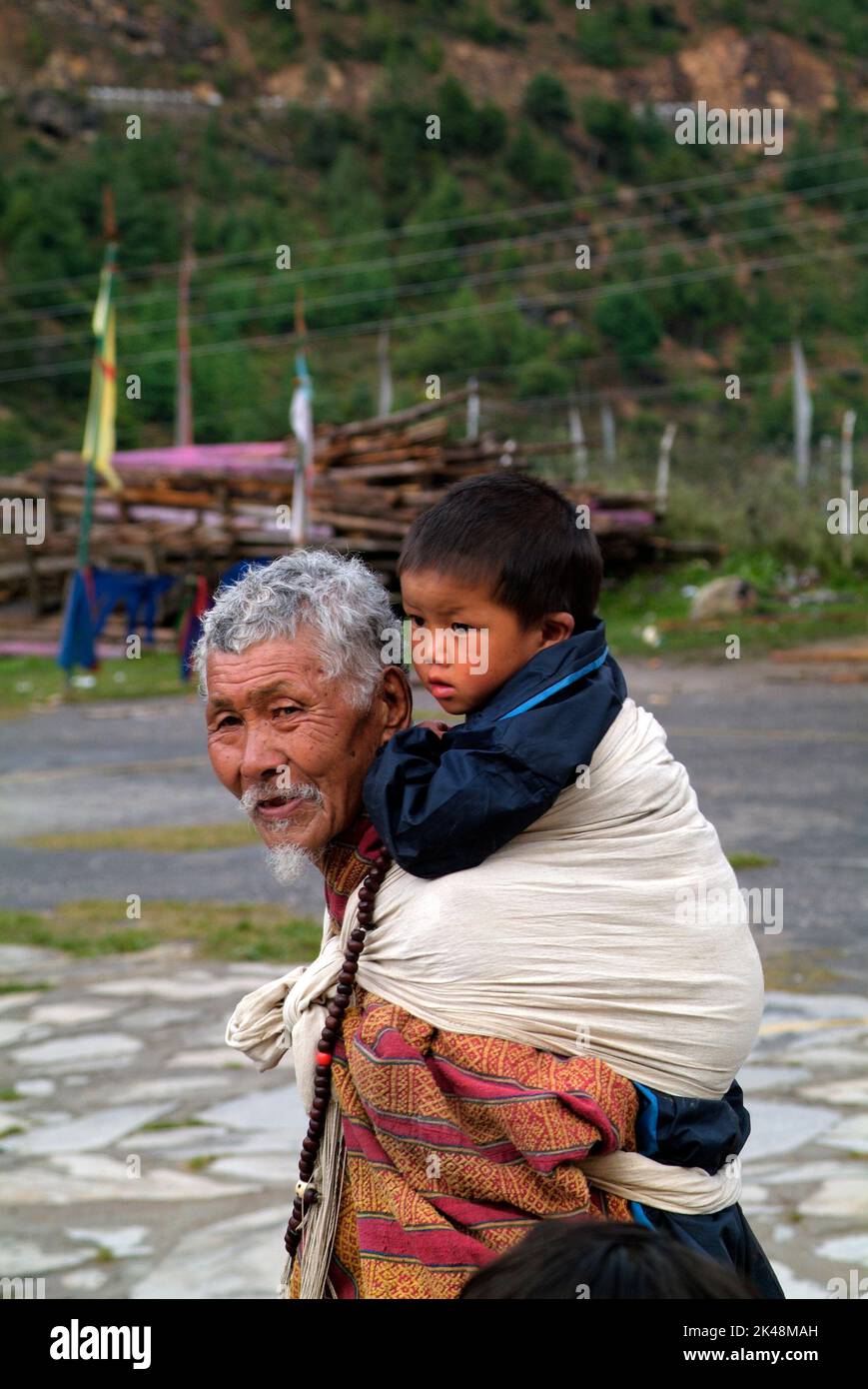 Haa, Bhutan - September 20,02007: Elder man wear on the back his grandchild in the tiny village in Haa valley Stock Photo