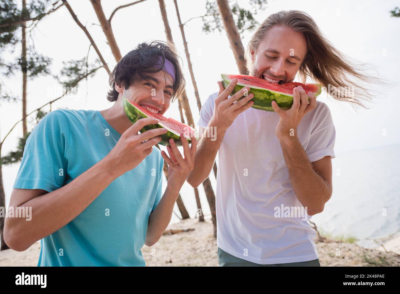 Photo of enjoy guys eat watermelon wear casual cloth outdoors on the river near trees Stock Photo