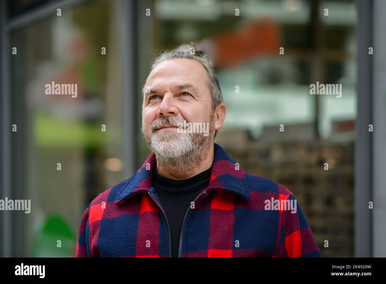 Middle aged man with a messy bun in a red and blue jacket in the style of a lumberjack stands in a shopping street Stock Photo