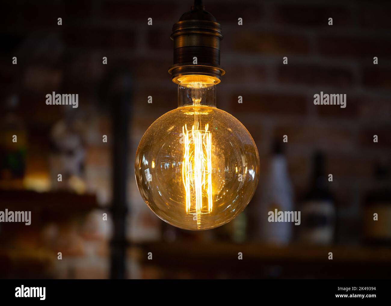 Light bulb with low energy filament illuminated lit up in dark room creating glowing light. Stock Photo