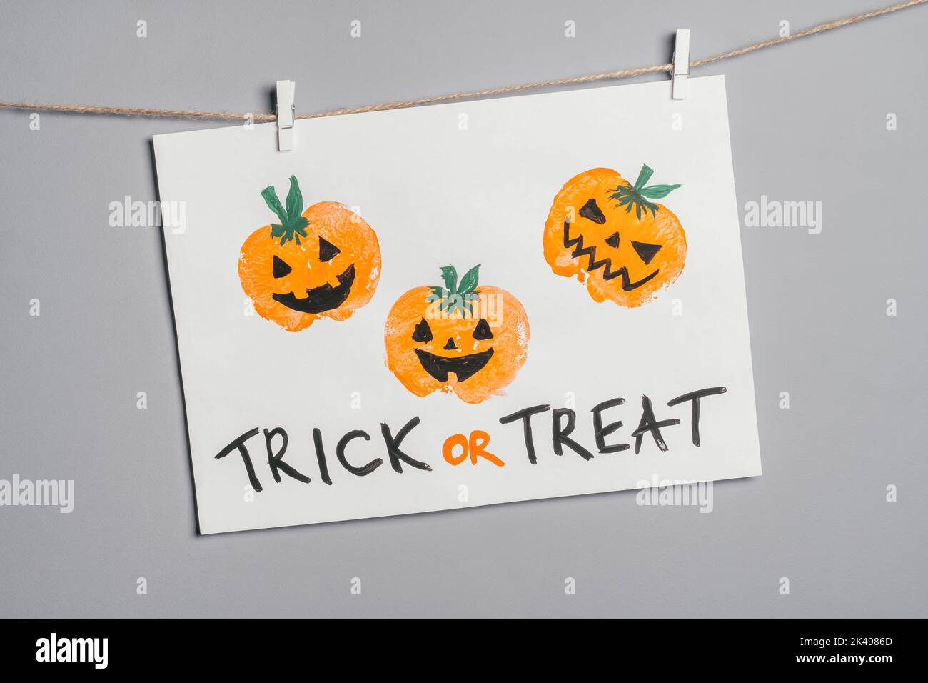 Halloween childrens pumpkin apple prints drawing hanging on rope on gray wall with Trick or Treat inscription. Handmade DIY decoration with children Stock Photo