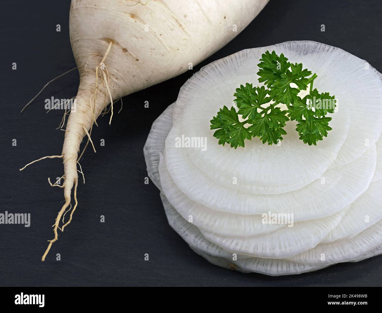 white radish thinly sliced on black slate board garnished with parsley, close up of fresh healthy root vegetable Stock Photo