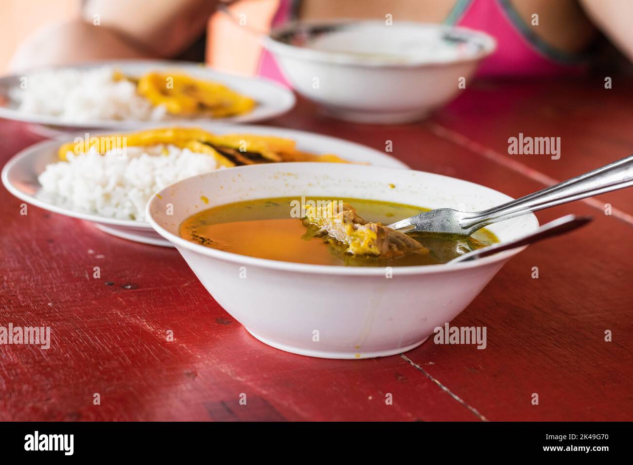 close-up of a typical Colombian dish of rib broth seasoned with natural spices and served on a red wooden table, in the background a peasant girl havi Stock Photo