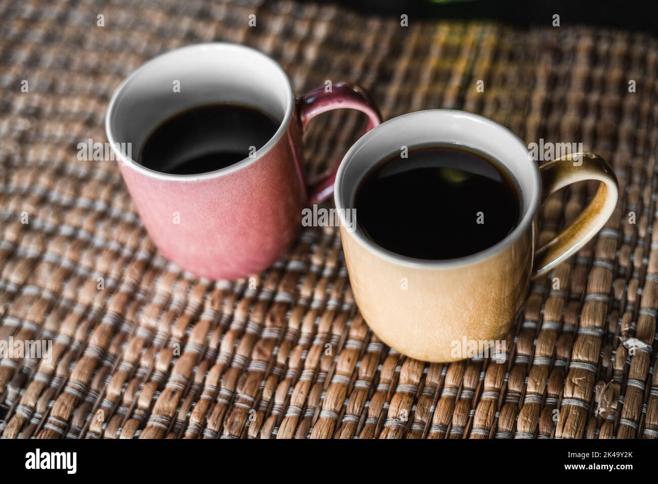 two porcelain cups on a wicker tablecloth one full and one half full coffee cup ready for breakfast Stock Photo