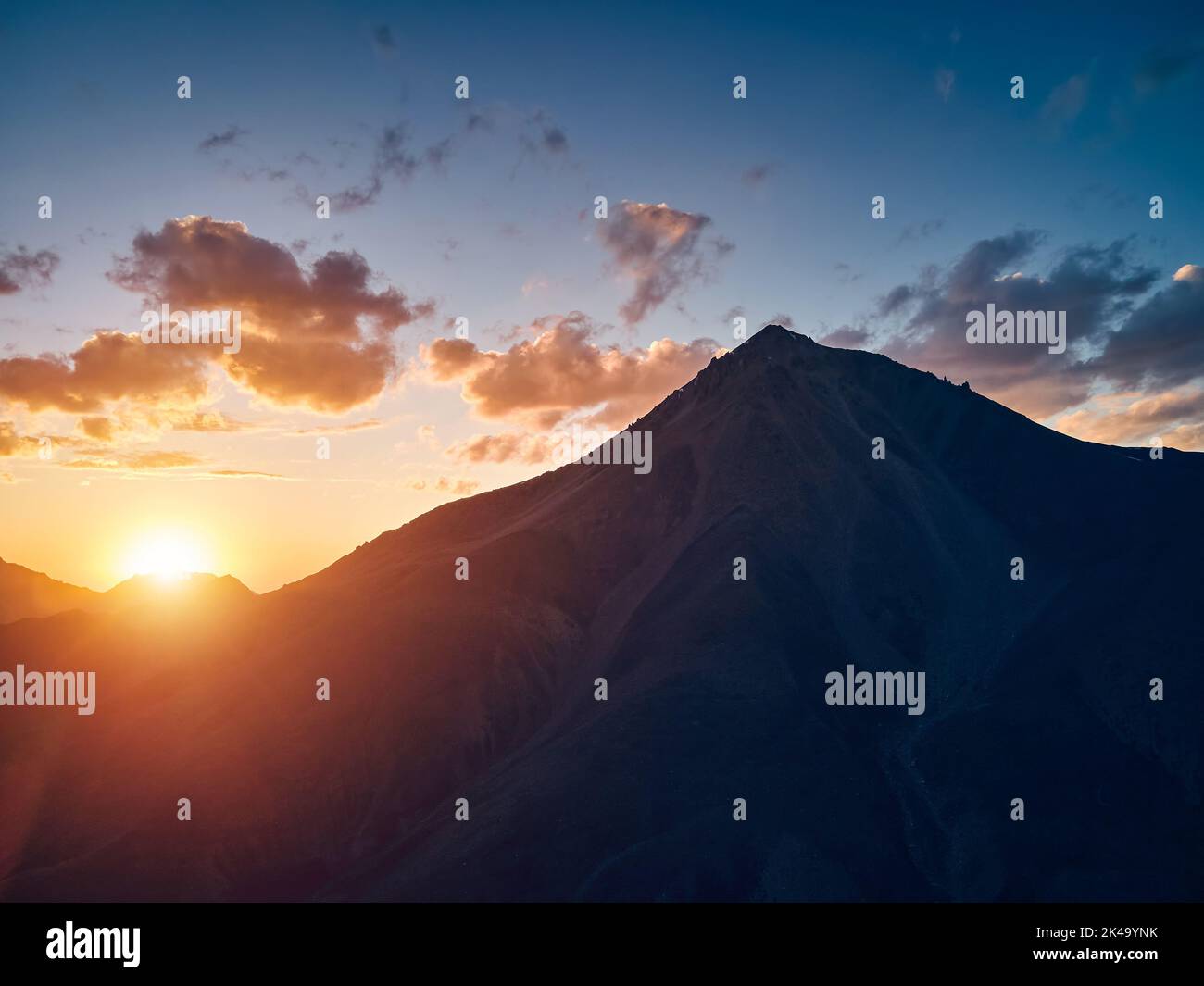 Beautiful scenery of the mountains summit in silhouette at orange sunset sky Almaty, Kazakhstan. Outdoor and hiking concept, aerial drone top shot Stock Photo