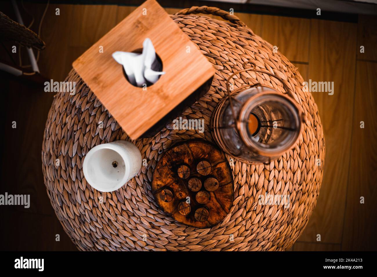 round wicker nightstand on a wooden floor with a tissue box a candle and a glass chandelier Stock Photo