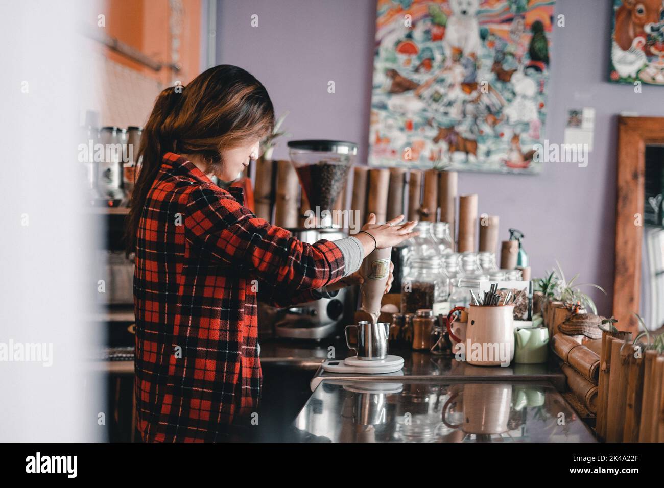 girl slapping glass bottle with palm and pouring cocoa milk into metal asian container on scale in clean and tidy coffee shop, the mylk bar, new Stock Photo