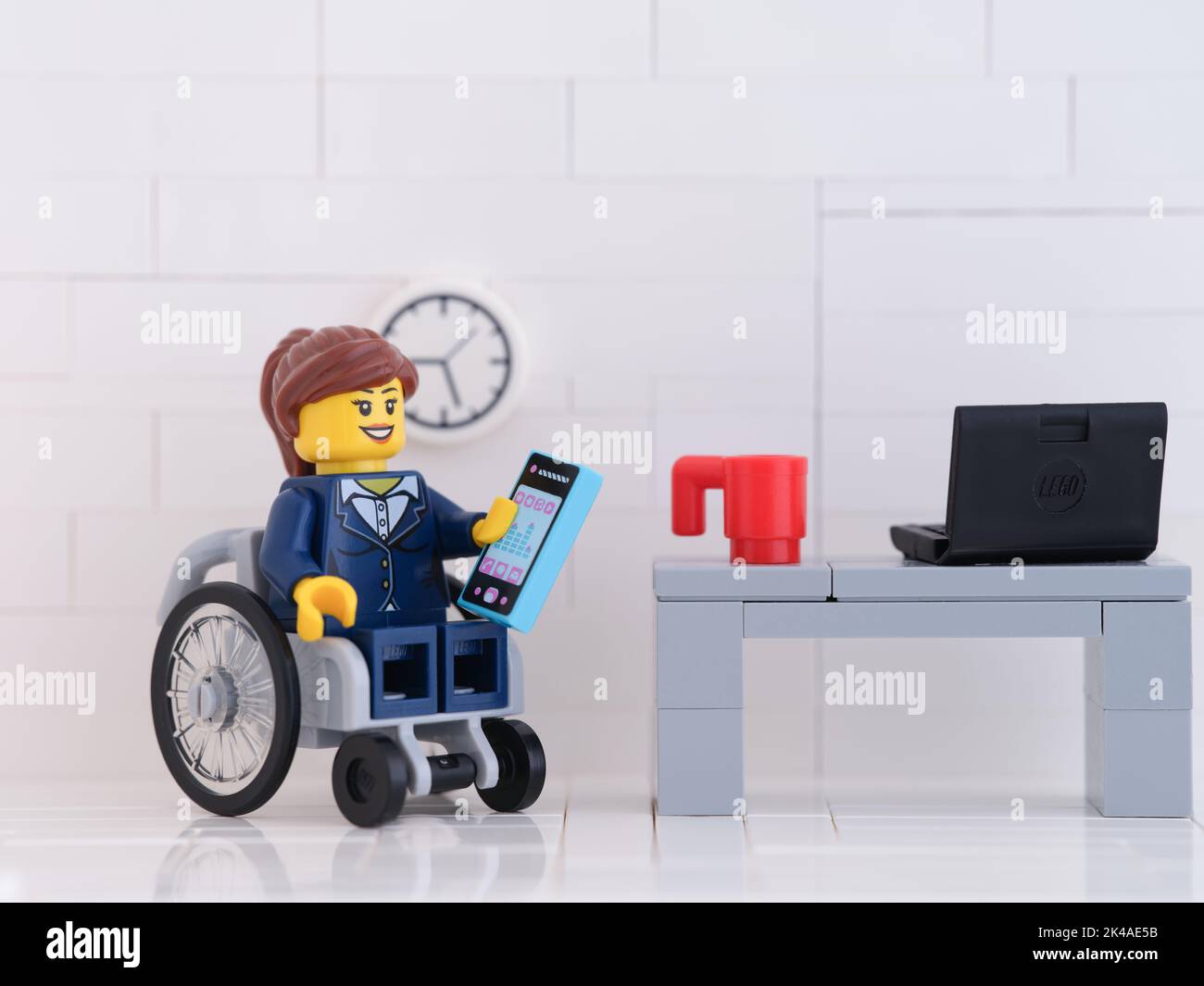 Tambov, Russian Federation - October 01, 2022 A Lego businesswoman minifigure in a wheelchair using a smartphone in her office. Stock Photo