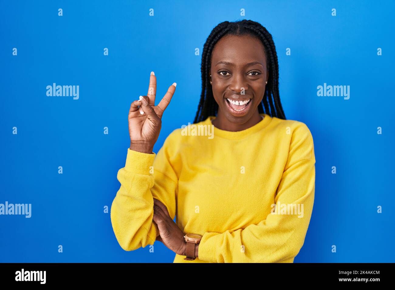 Beautiful black woman standing over blue background smiling with happy ...