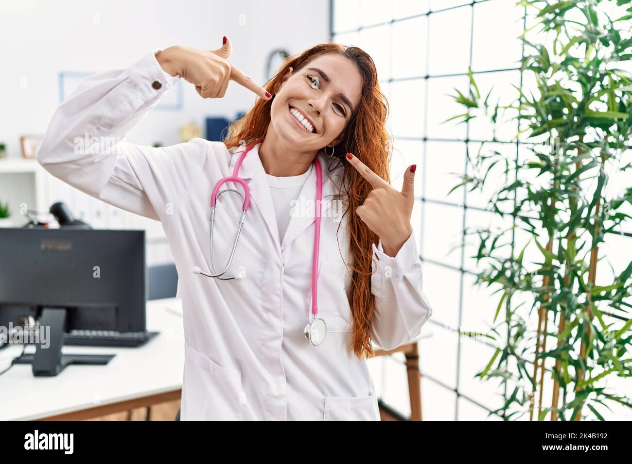 Young redhead woman wearing doctor uniform and stethoscope at the clinic smiling cheerful