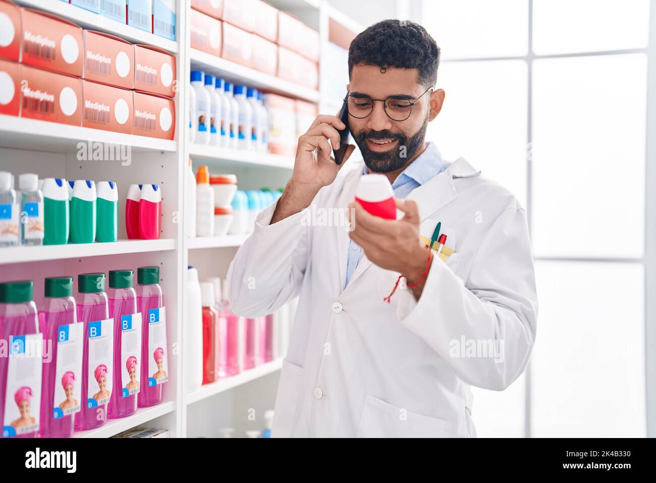 Young arab man pharmacist holding toothpaste bottle talking on ...