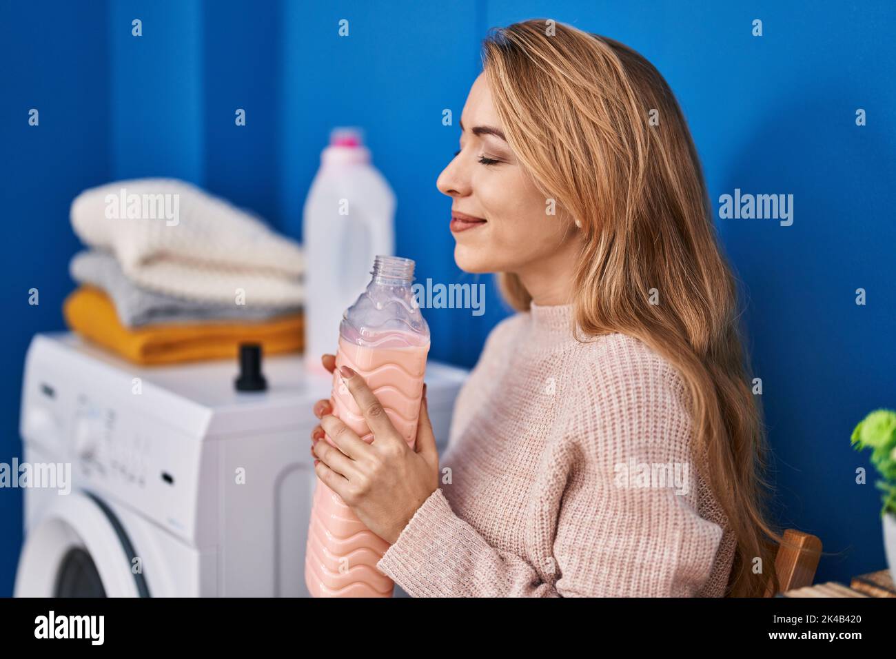 Young woman smelling detergent waiting for washing machine at laundry