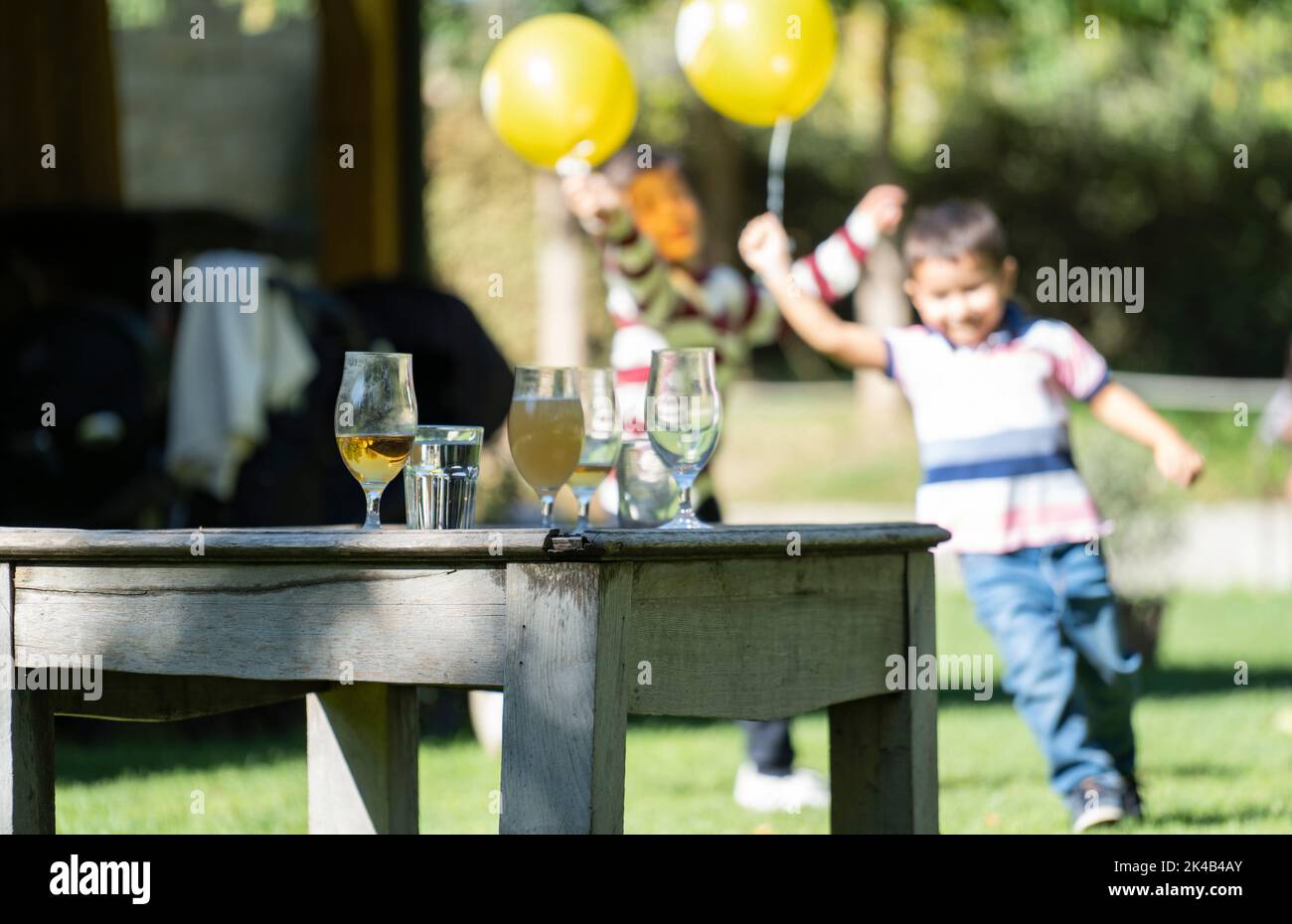 Glasses with drinks on a vintage table during a party. Happy children running with yellow balloons on blurred background Stock Photo