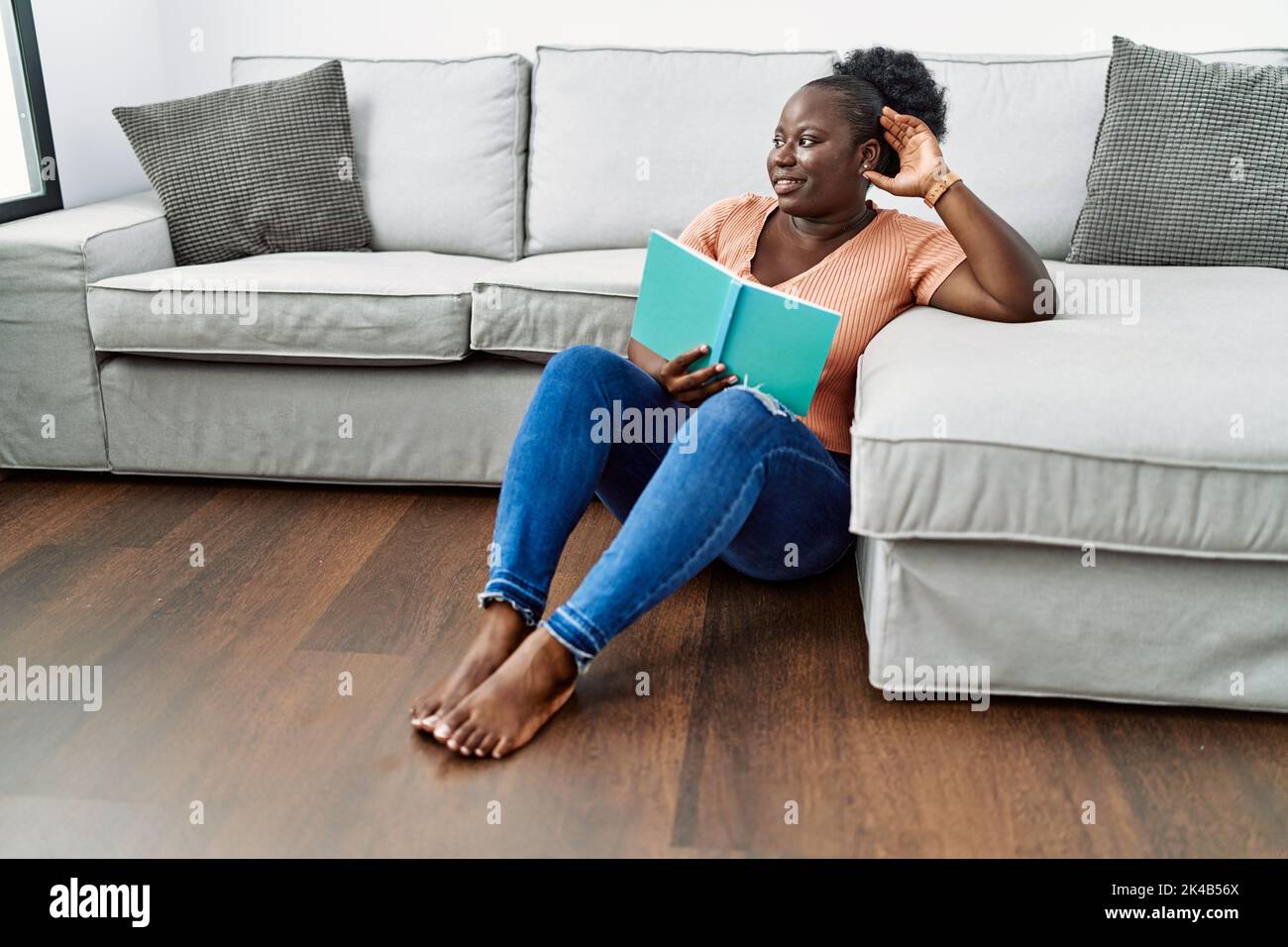 Young african american woman reading book sitting on the floor at home ...