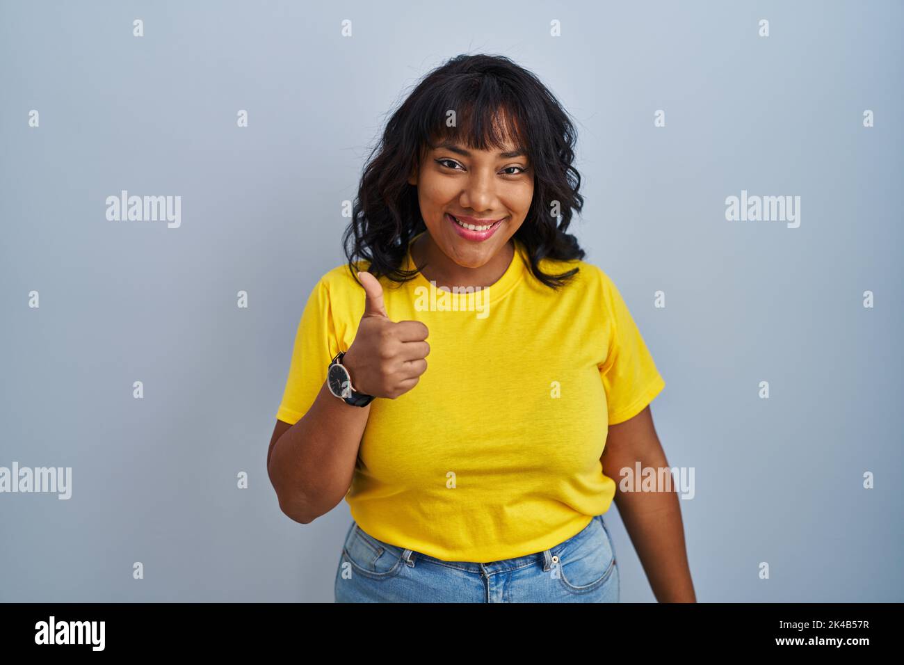 Hispanic woman standing over blue background doing happy thumbs up ...