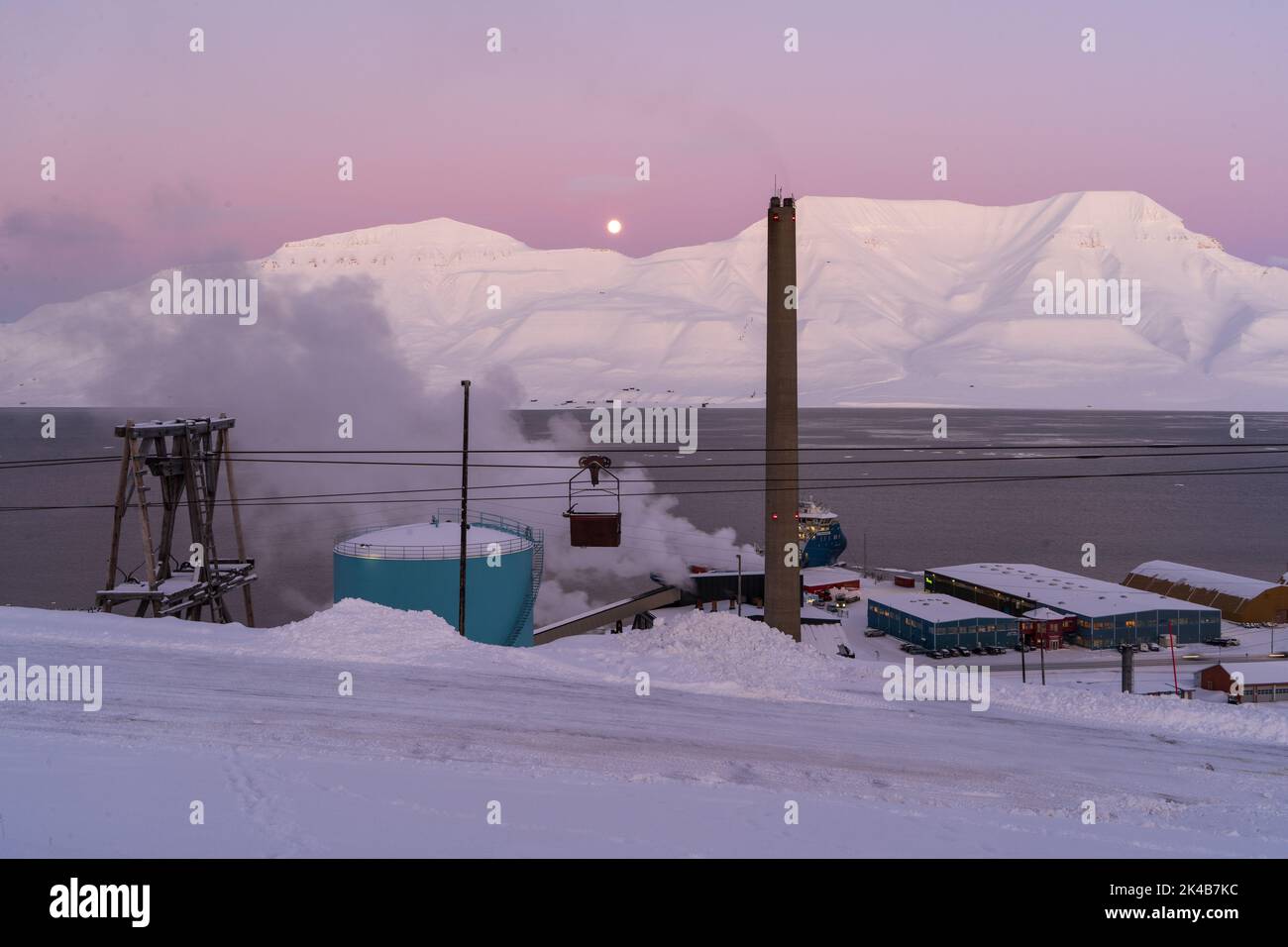 Coal power plant chimney and surrounding industrial area during pink purple dusk sunset on snow winter day, Longyearbyen, Svalbard Stock Photo