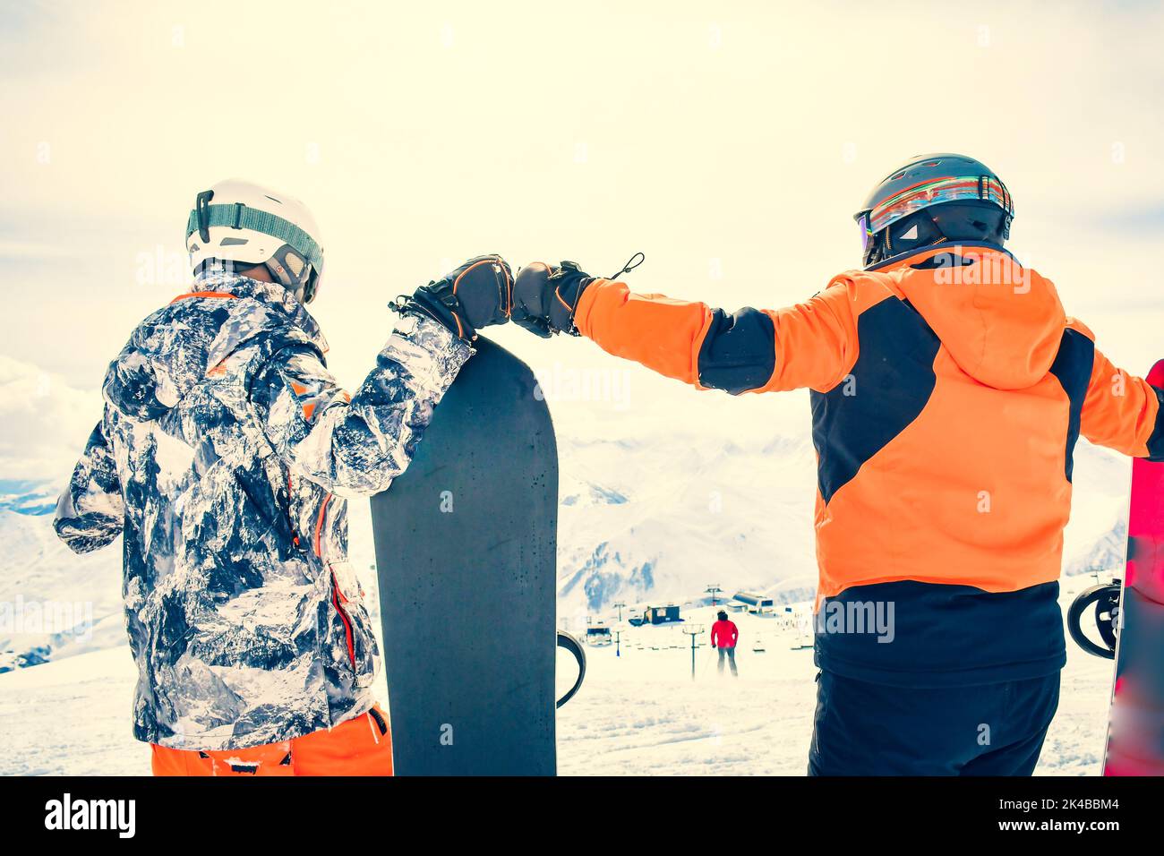 two cool snowboarders low angle back view punch fists with mountains panorama. Fun holidays outdoors in ski resort Stock Photo