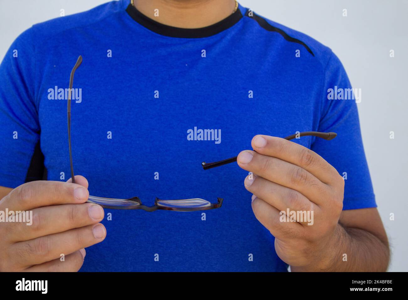 Image of a man holding a pair of broken eyeglasses. Breaking the temple of the glasses of a short-sighted boy Stock Photo