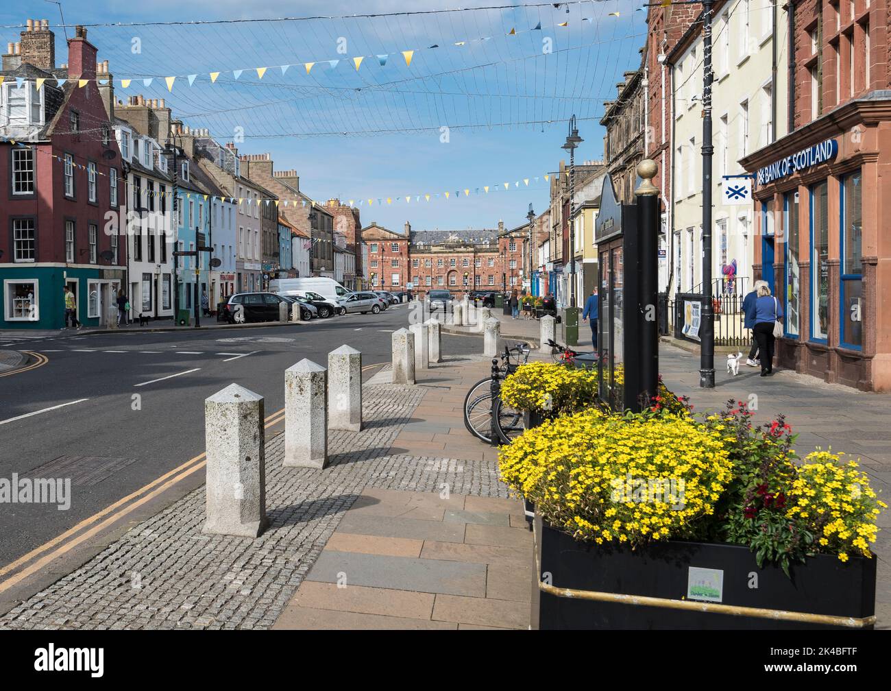 Dunbar High Street with flowering planters in foreground with yellow and blue bunting under a blue sky on a sunny day. Stock Photo