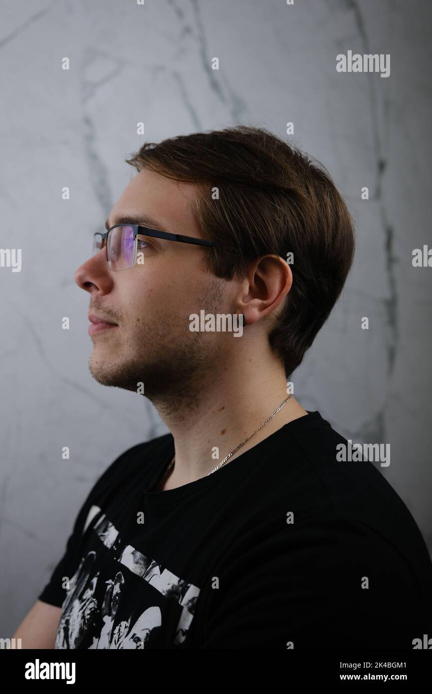 Unshorn and unshaven guy in glasses and black tshirt with long hair on gray background. Stock Photo