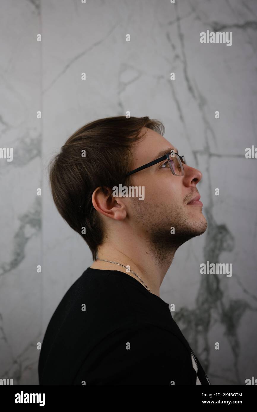 Unshorn and unshaven guy in glasses and black tshirt with long hair on gray background. Stock Photo