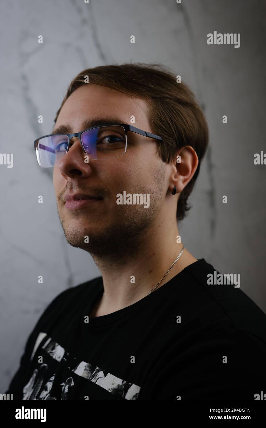 Unshorn and unshaven guy in glasses and black tshirt with long hair on gray background. Stock Photo