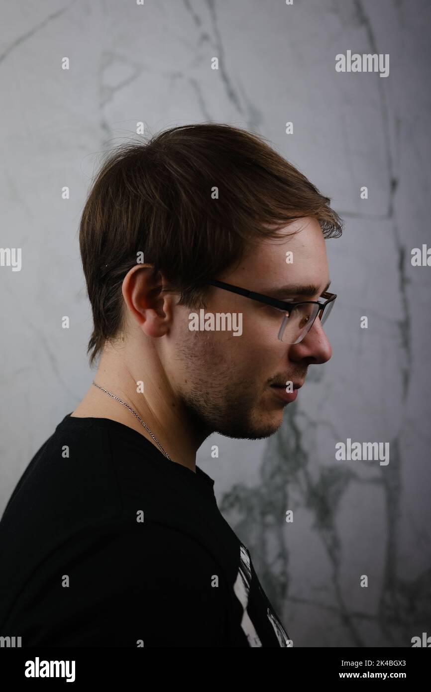 Unshorn and unshaven guy in glasses and black tshirt with long hair on gray background. Stock Photo