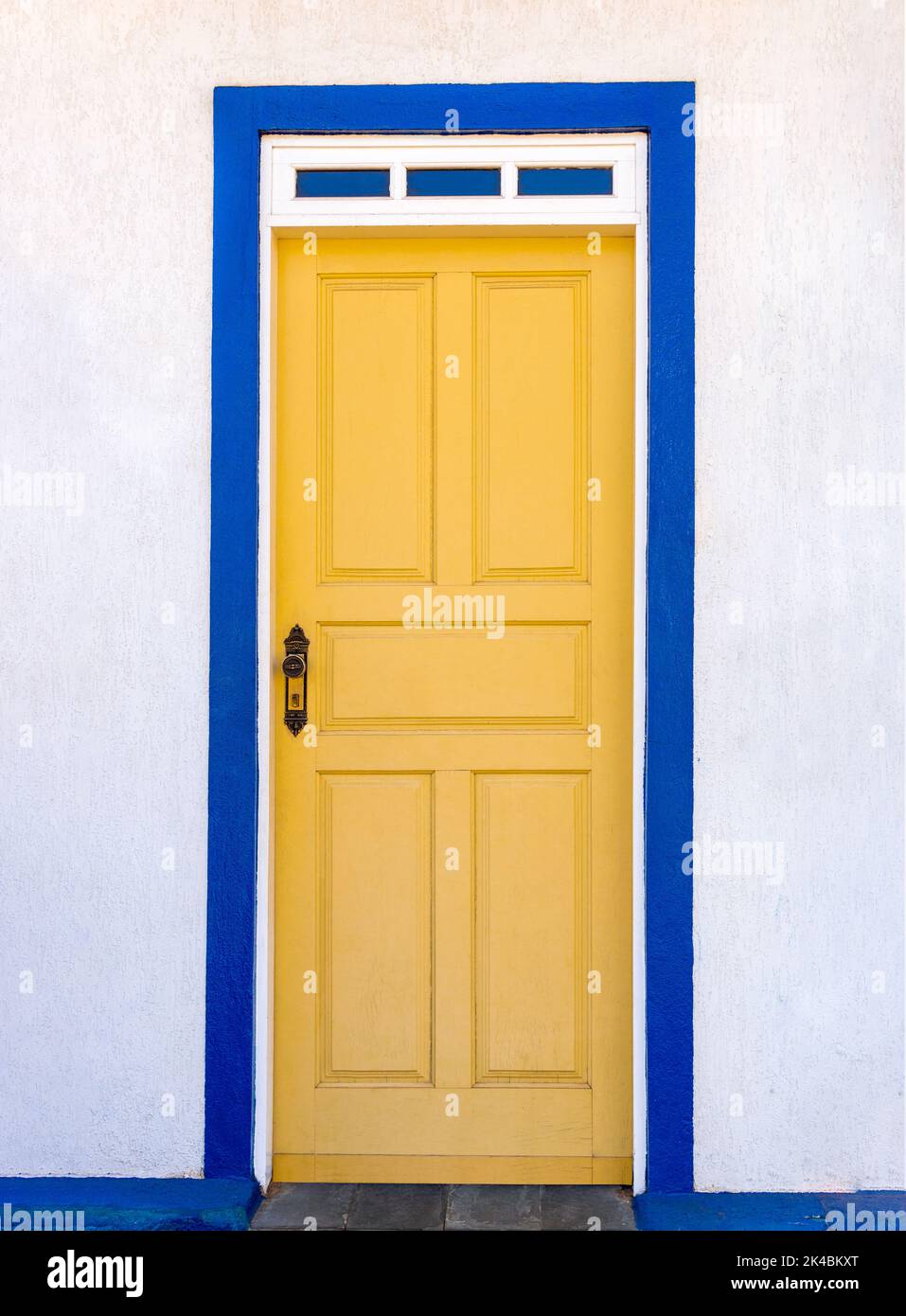 Wood paneled door painted in yellow with cobalt blue and white trim in Sabará, Minas Gerais, Brazil Stock Photo