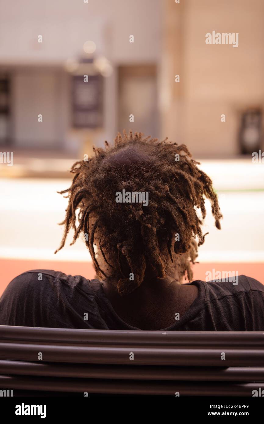 A vertical back shot of a black male sitting on the bench in the street ...