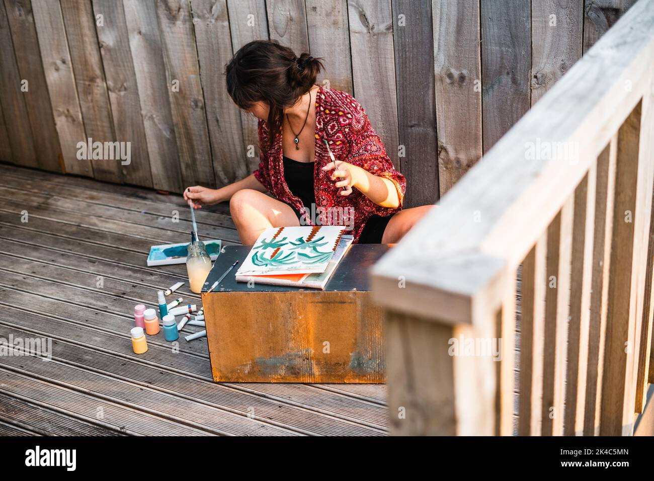 Young woman painter sitting on the floor dipping the brush in the ...