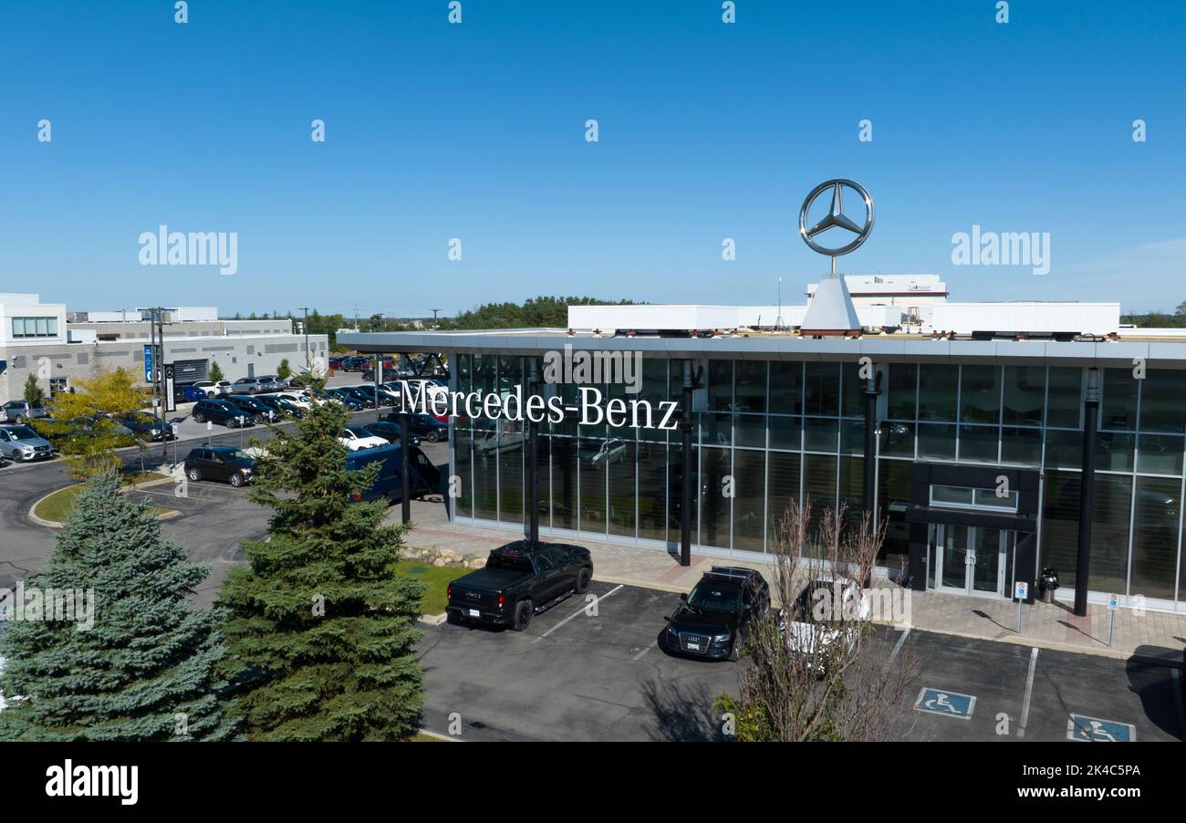 An aerial view out front of a modern Mercedes-Benz dealership, the famous Mercedes star emblem shining in the sun on a blue sky day. Stock Photo