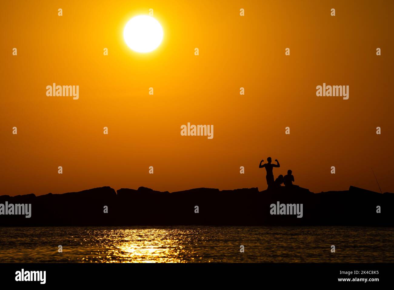 A beautiful shot from the sea of silhouettes of people on land in the sunset Stock Photo