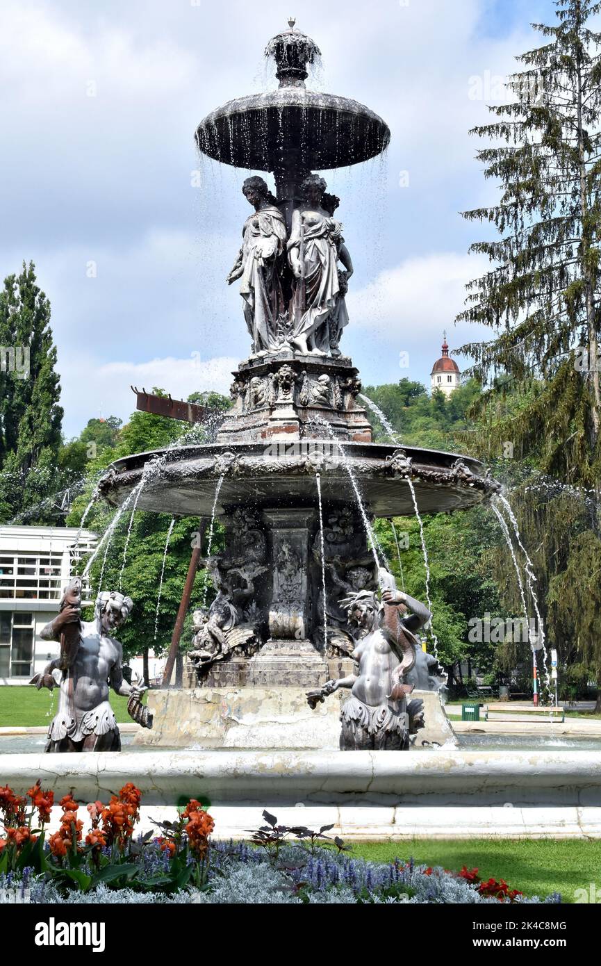 The vertical view of vintage fountains and trees in Stadtpark Graz under the blue cloudy sky Stock Photo