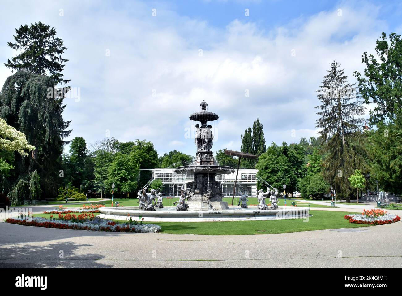 The view of vintage fountains and trees in Stadtpark Graz under the blue cloudy sky Stock Photo