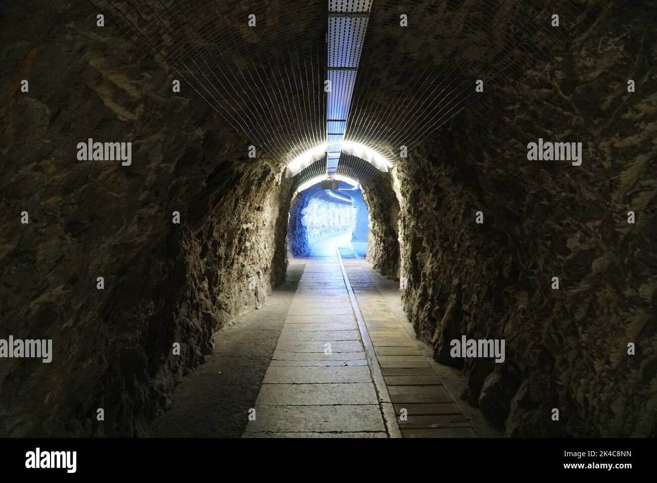 An inside view of an old underground tunnel with a blue light at the end Stock Photo