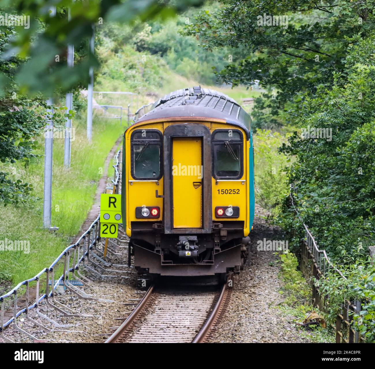 The high-angle view of an old yellow train over the rails passing through the greenery Stock Photo