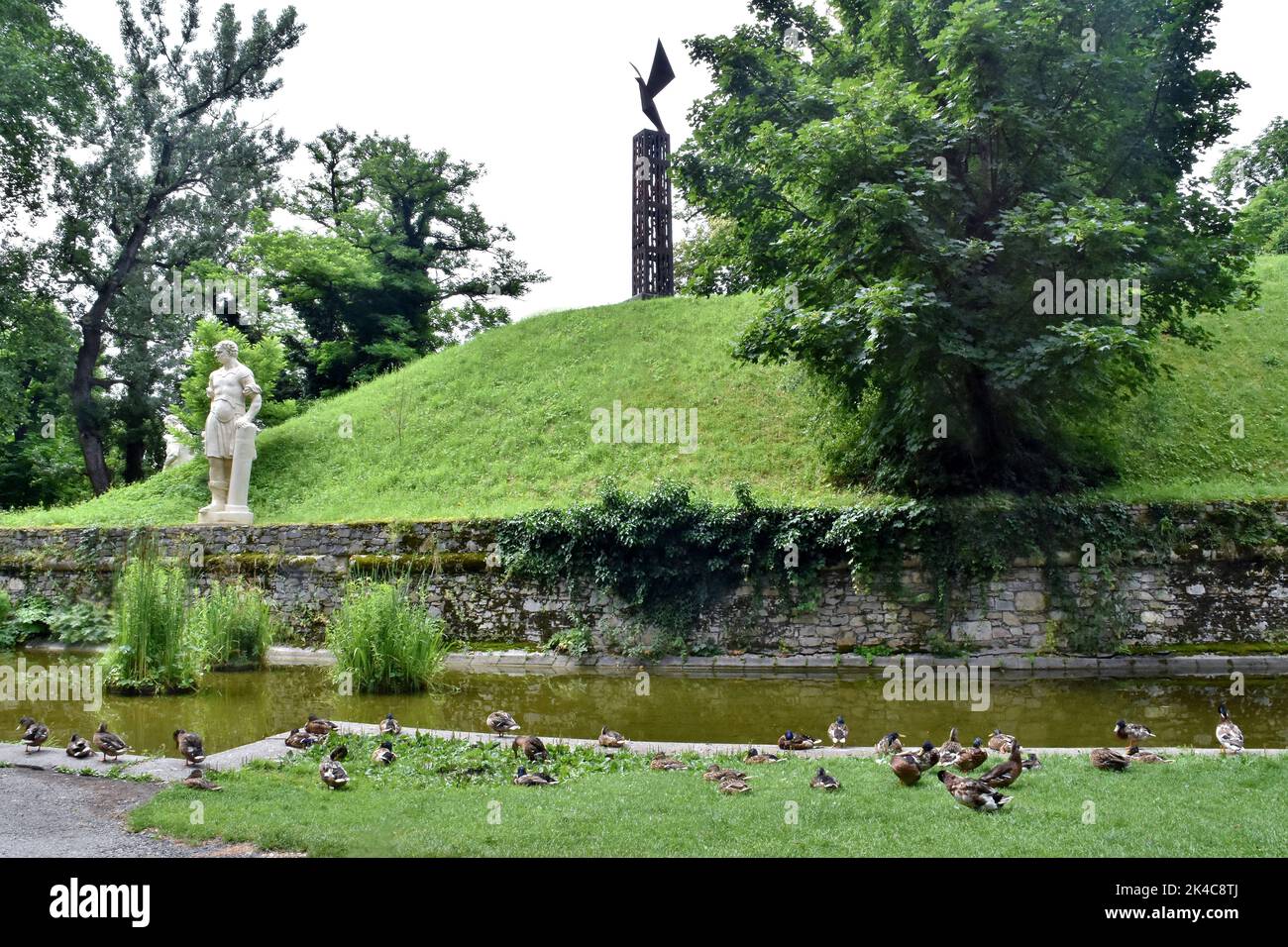 The view of trees and sculptures by the pond in the Graz Stadtpark on a sunny day Stock Photo