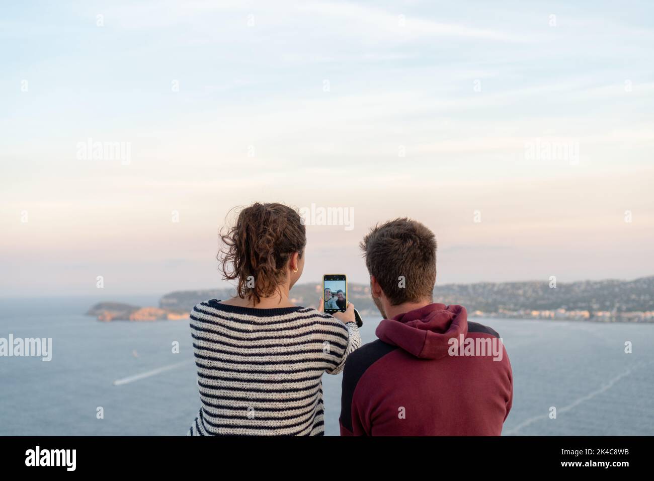 A couple sitting and taking selfies with the beautiful seascape at sunset Stock Photo