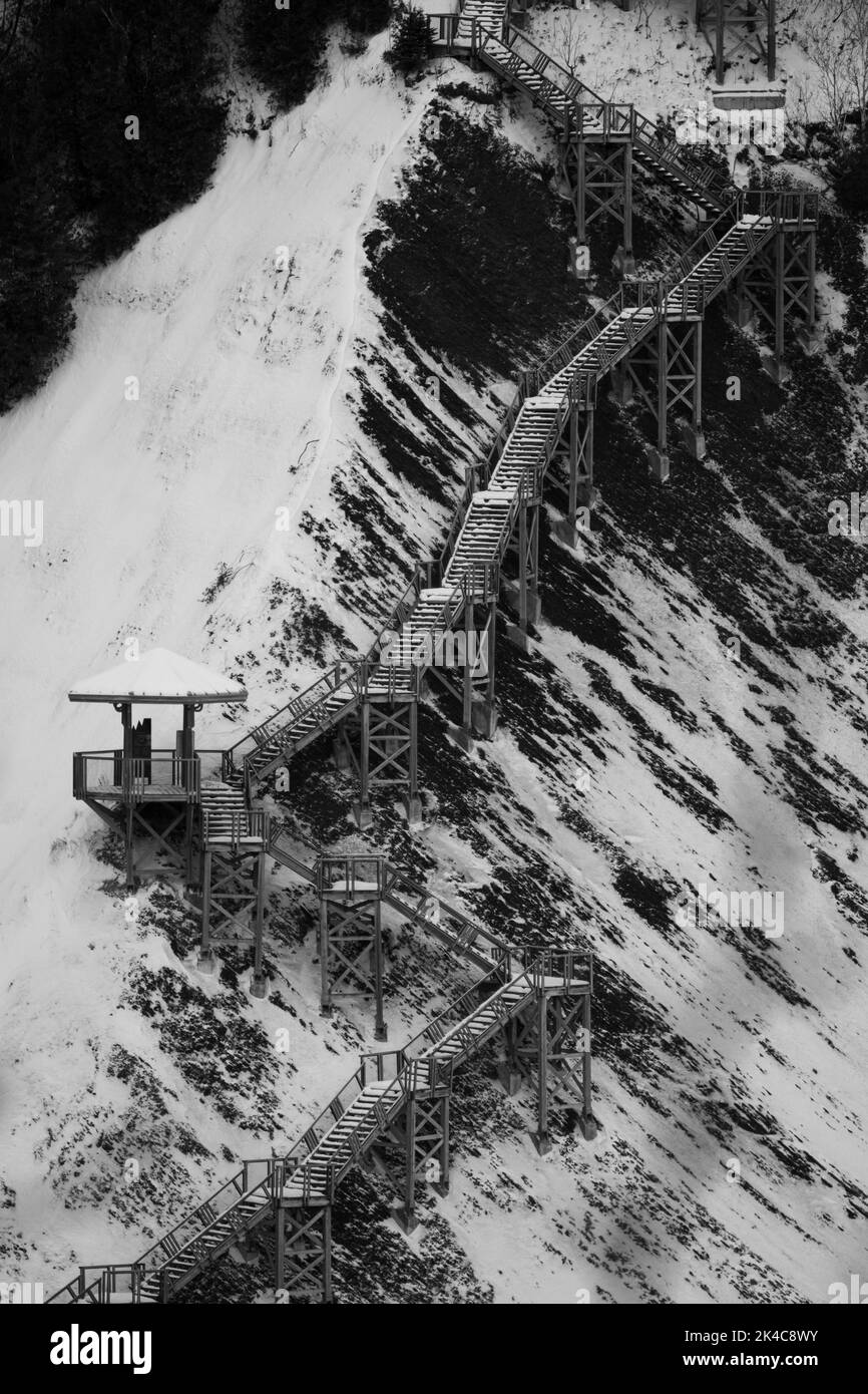 A vertical shot of a stairway on a snow-covered mountain slope in grayscale Stock Photo