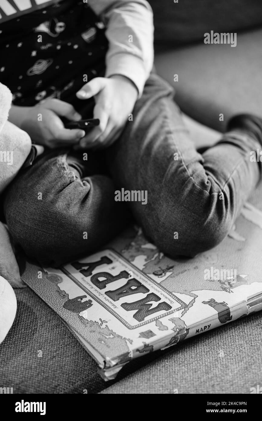 A grayscale shot of a young boy sitting on a Polish atlas for children called Mapy on a couch Stock Photo