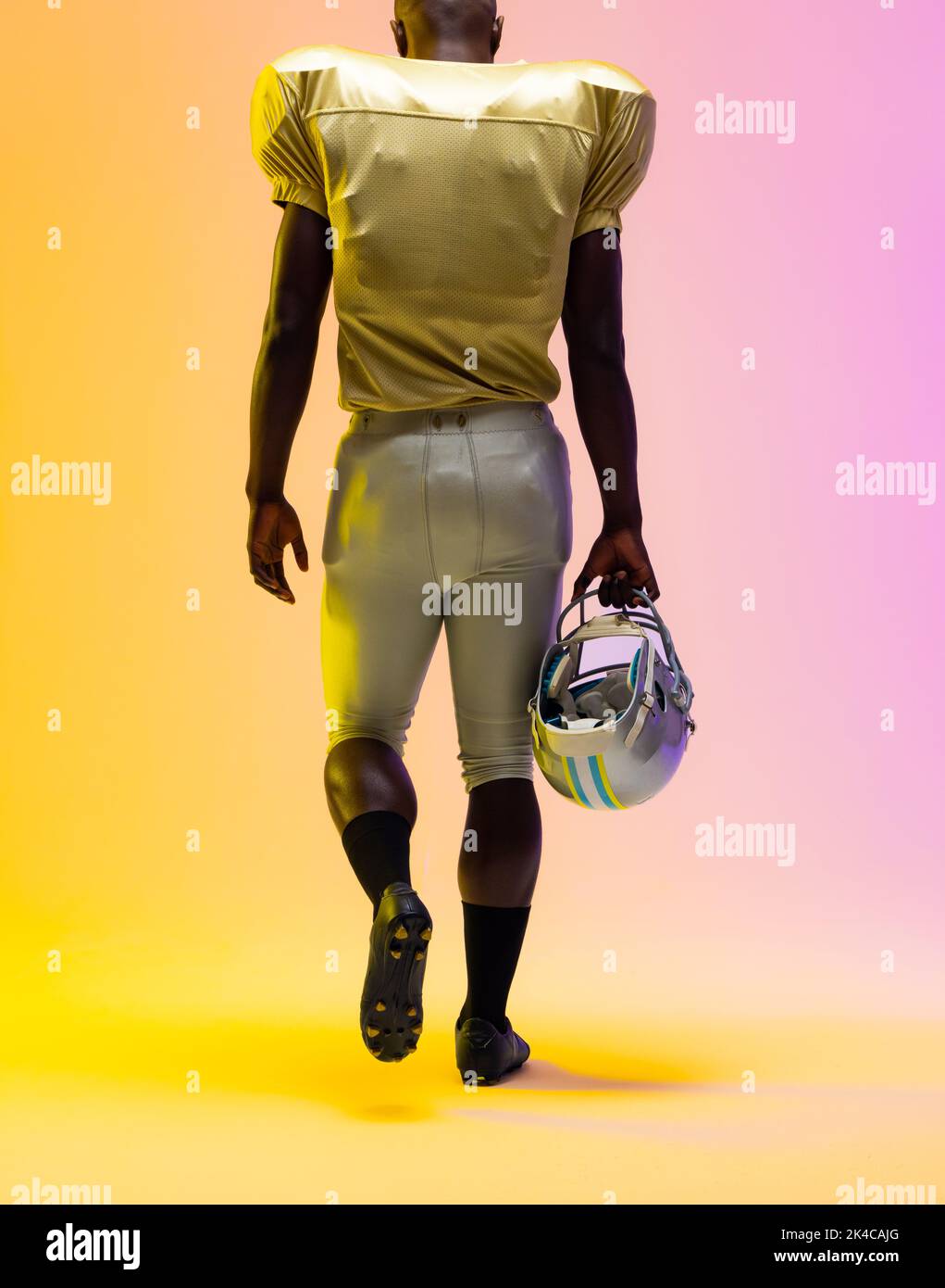 African american male american football player holding helmet with neon yellow and purple lighting. Sport, movement, training and active lifestyle con Stock Photo