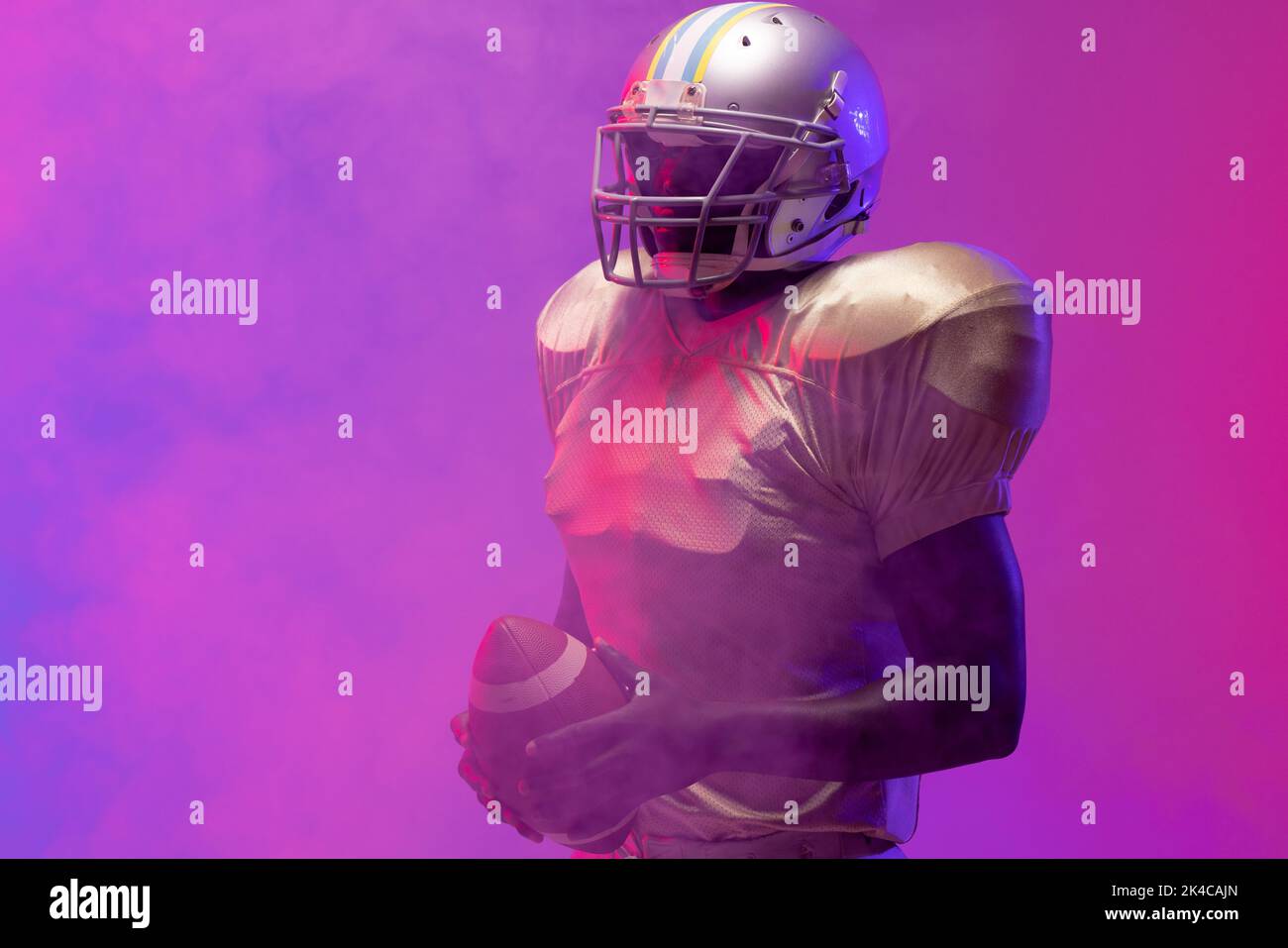 African american male american football player holding ball with neon purple and pink lighting. Sport, movement, training and active lifestyle concept Stock Photo