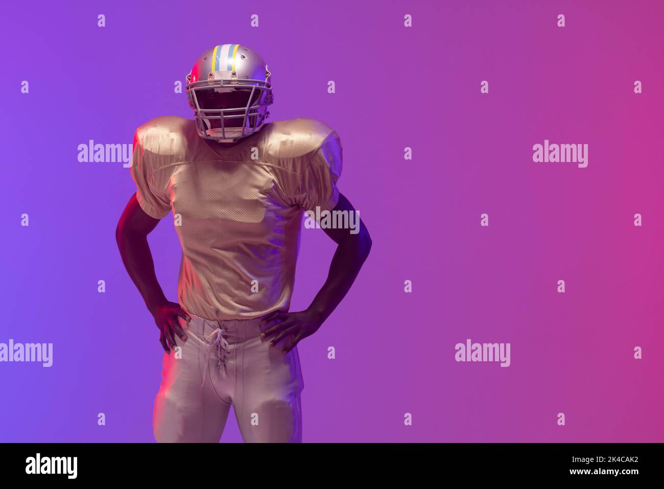 African american male american football player wearing helmet with neon blue and purple lighting. Sport, movement, training and active lifestyle conce Stock Photo