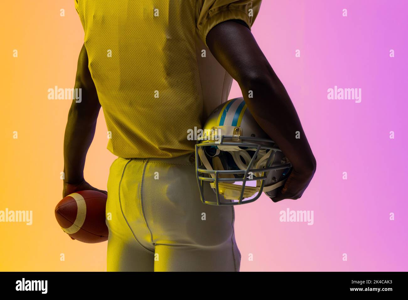 Midsection of african american male american football player with neon purple and yellow lighting. Sport, movement, training and active lifestyle conc Stock Photo