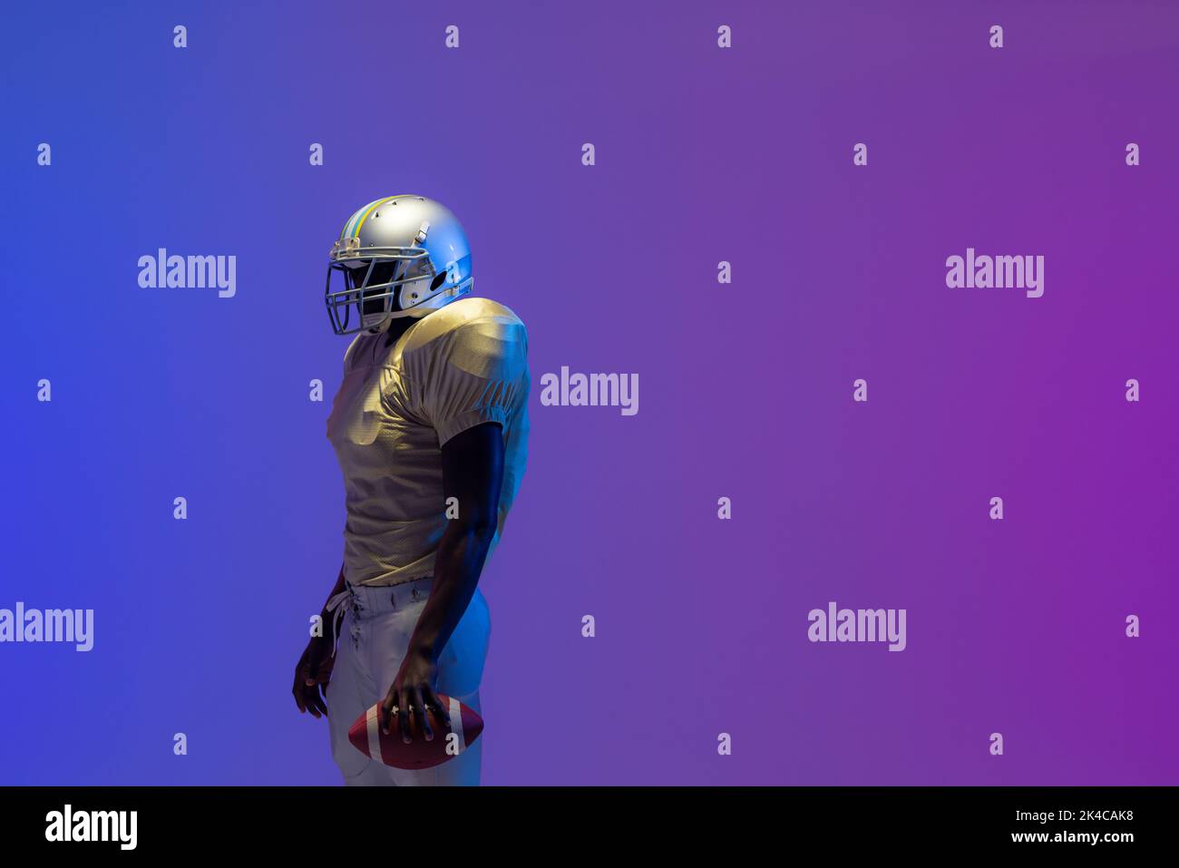African american male american football player holding ball with neon blue lighting. Sport, movement, training and active lifestyle concept. Stock Photo