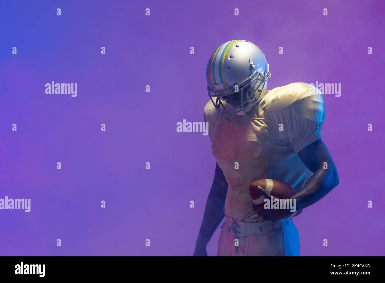 African american male american football player holding ball with neon blue lighting. Sport, movement, training and active lifestyle concept. Stock Photo