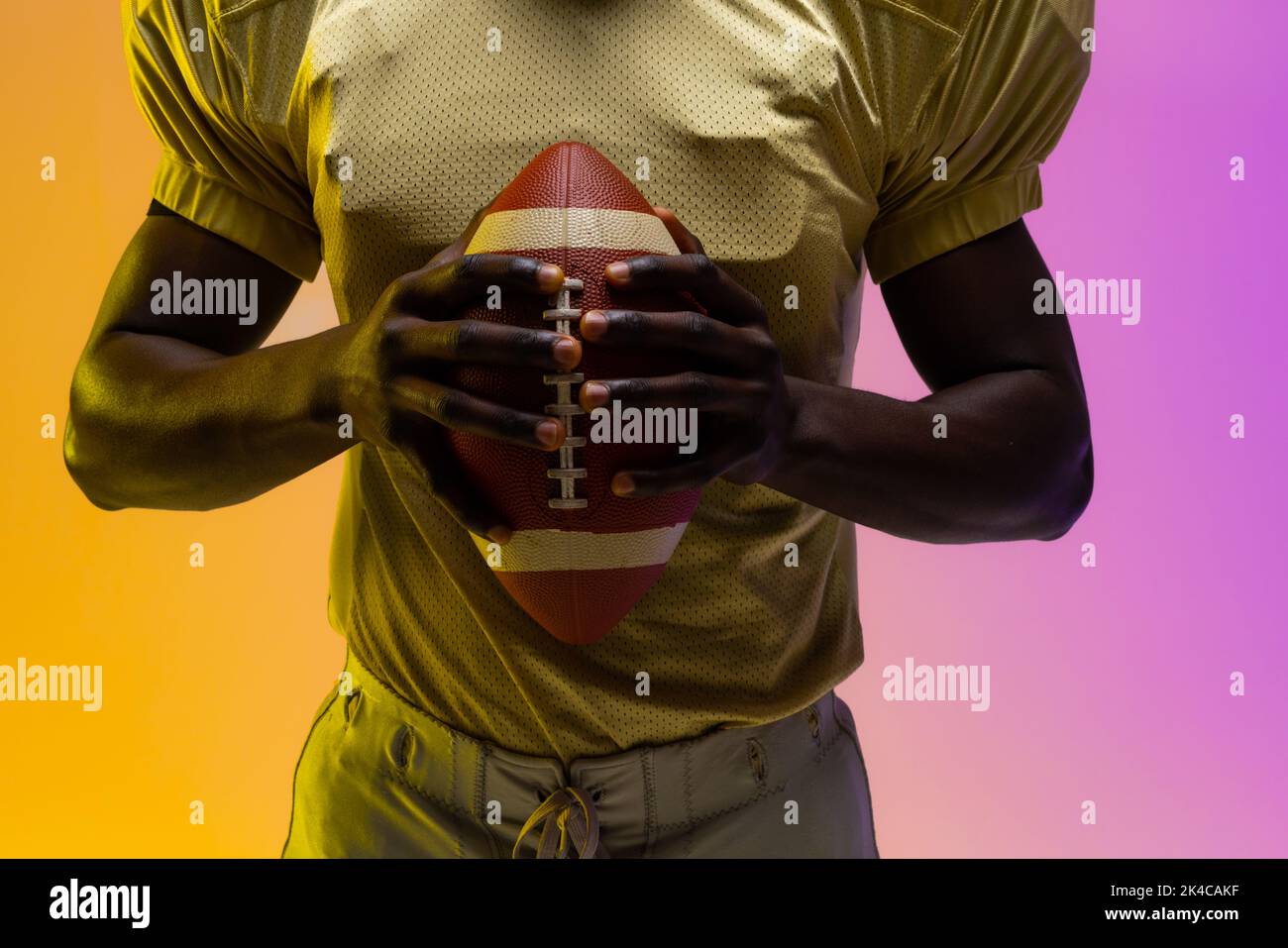 Midsection of african american male american football player with neon purple and yellow lighting. Sport, movement, training and active lifestyle conc Stock Photo