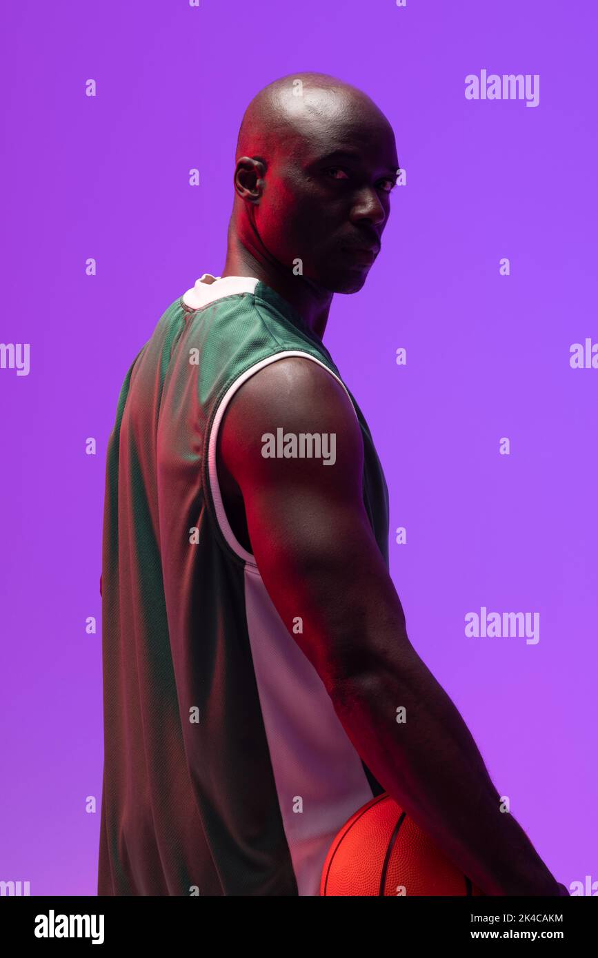 Image of portrait of african american basketball player with basketball on neon purple background. Sports and competition concept. Stock Photo